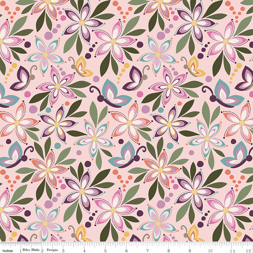 Juju's Petals Floral Pink quilting fabric shown with a ruler for scale, featuring colorful flowers, butterflies, and olive green leaves on a soft pink background.