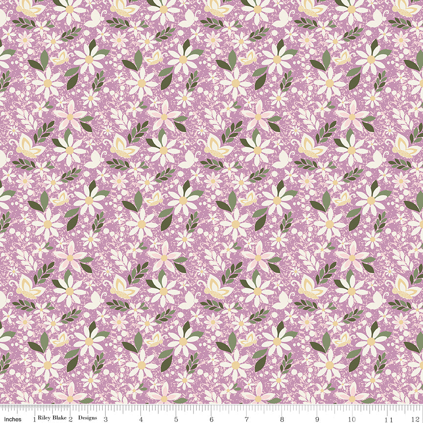 Juju's Petals Dance Lilac floral quilting fabric shown with a ruler for scale, featuring cream daisies, pink blossoms, and green foliage on a lilac background.